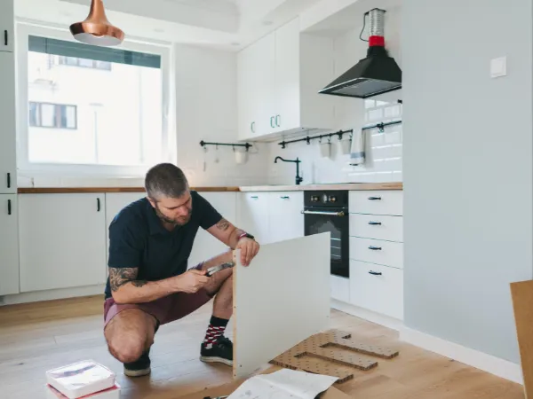 A man kneels on the floor, assembling kitchen furniture in a modern space