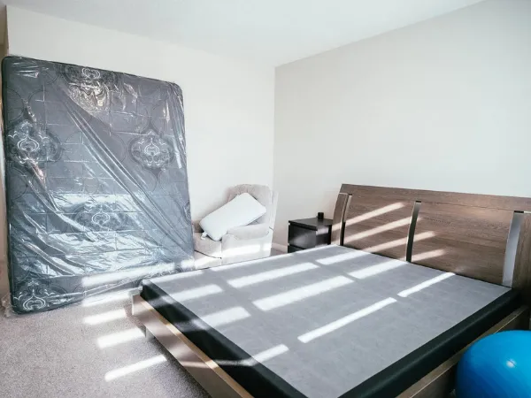 A partially furnished room features a bed frame, a mattress leaning against the wall, and a blue exercise ball