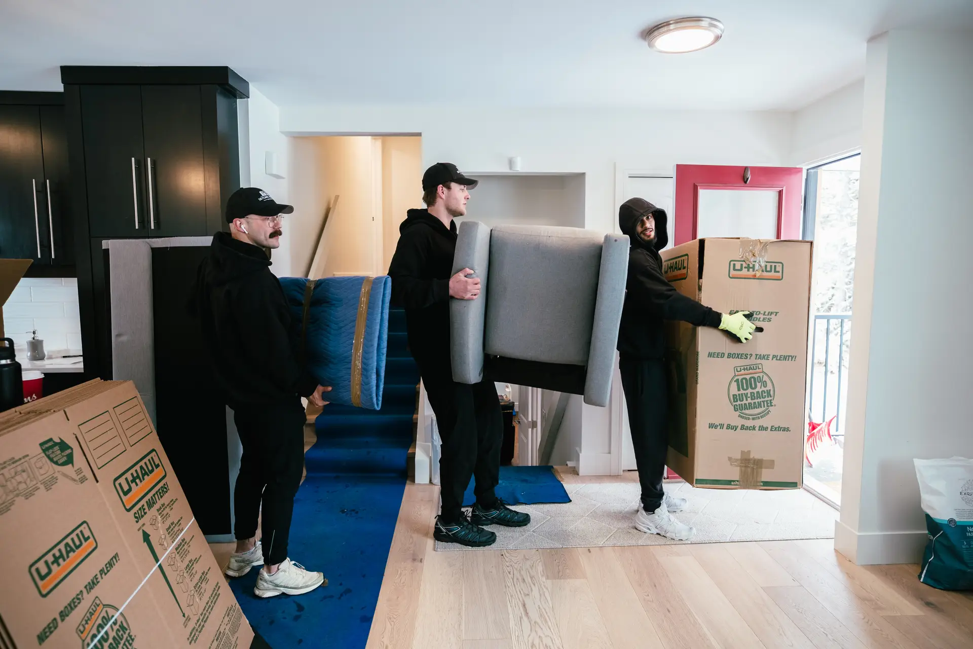 Three individuals are moving furniture and boxes in a bright, empty room