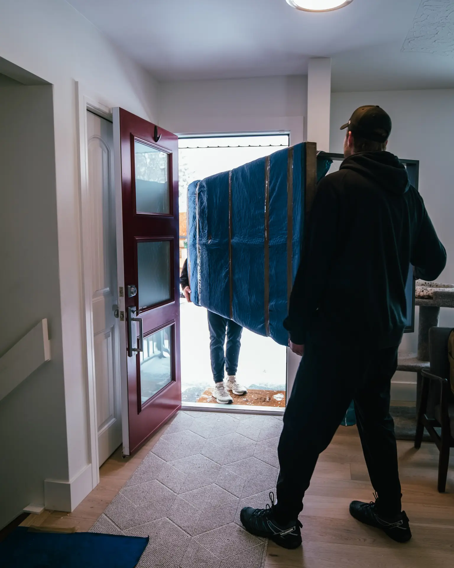 A person carries a large, blue-wrapped item through a doorway