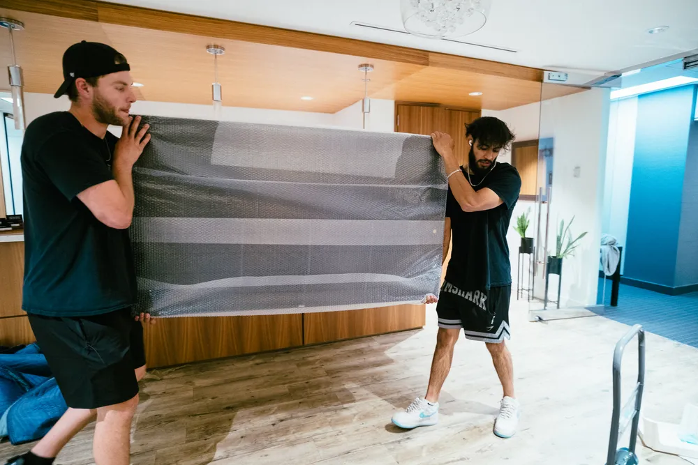Two men are lifting and carrying a large, wrapped object in a modern interior space