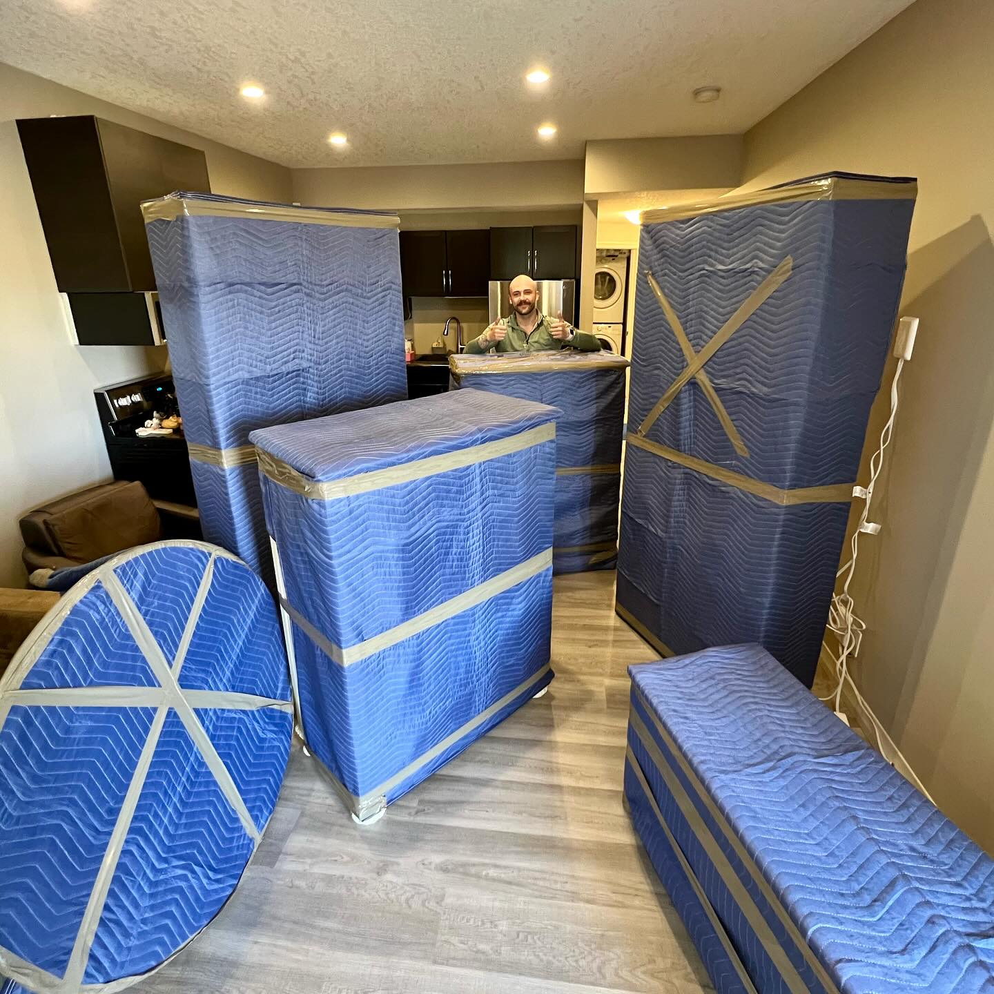 Several large, blue-wrapped furniture pieces occupy a spacious, well-lit room